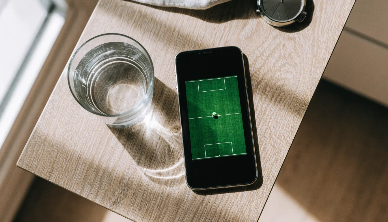 Ein Smartphone liegt mit dem Display nach unten auf einem Küchentisch, daneben stehen ein Glas Wasser und eine Armbanduhr.