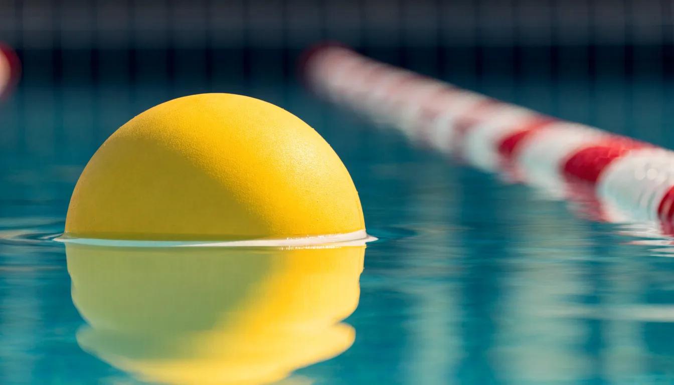 Ein gelber Wasserball treibt in Nahaufnahme auf der Wasseroberfläche neben einer Leine mit Bojen.