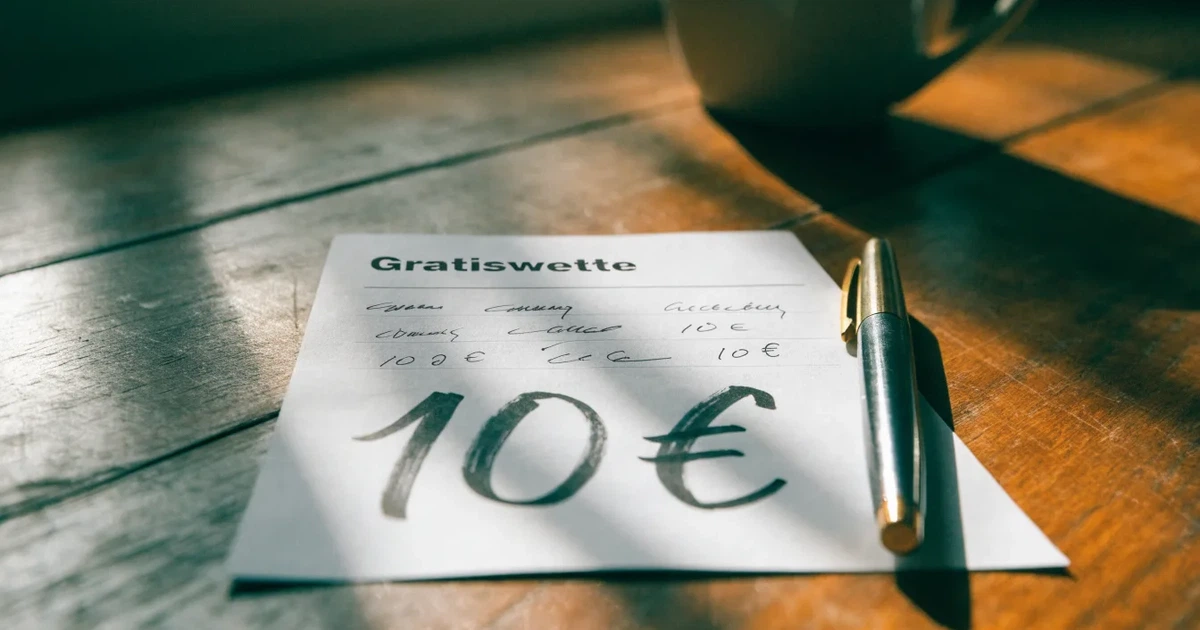 Ein leerer Papier-Wettschein und ein Kugelschreiber liegen auf einem Holztisch, daneben ein kleiner Stapel Münzen im Morgenlicht.
